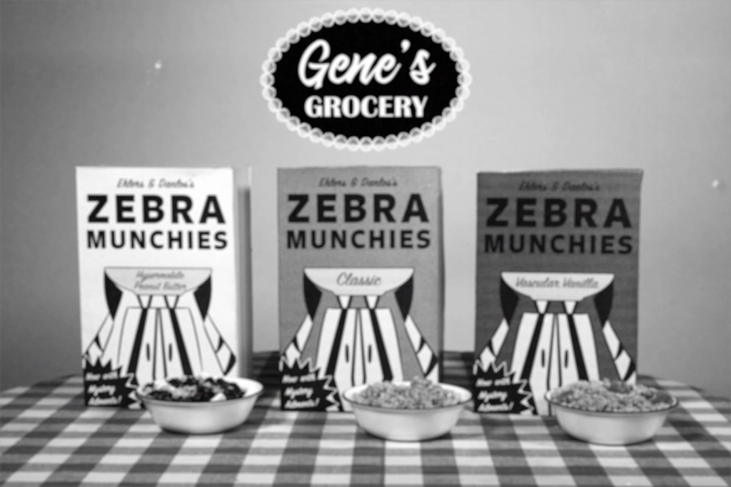 Three cereal boxes for the fake cereal brand Ehlers and Danlos's Zebra Munchies sit on a table. Each box shows a cartoon zebra holding a bowl. In front of each box is a bowl of cereal. Above the cereal boxes is a logo for a fake grocery store "Gene's Grocery". The image is digitally aged.